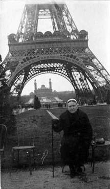 Iconographie - Femme âgée portant la coiffe, posant assise devant la Tour Eiffel